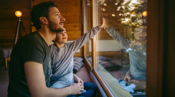 Vater und Sohn blicken gemeinsam durch eine große Fensterscheibe ins Freie
