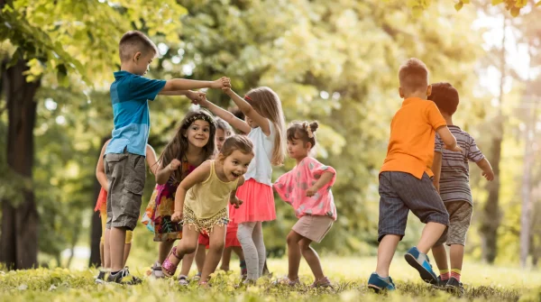Fröhlich spielende Kinder im Park, die gemeinsam einen Kreis bilden – Symbol für Gesundheit, Bewegung und Unbeschwertheit.