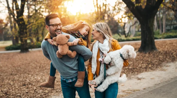 Eine fröhliche Familie mit Kind und Hund beim Spaziergang im Park – Symbol für Sicherheit, Zusammenhalt und familiären Schutz