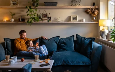 Vater und Tochter sitzen entspannt auf dem Sofa im Wohnzimmer und schauen gemeinsam auf ein Smartphone