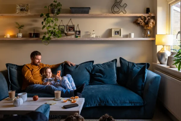 Vater und Tochter sitzen entspannt auf dem Sofa im Wohnzimmer und schauen gemeinsam auf ein Smartphone