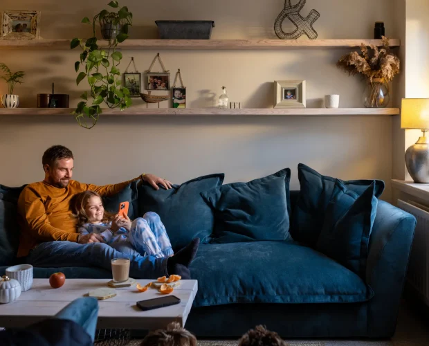 Vater und Tochter sitzen entspannt auf dem Sofa im Wohnzimmer und schauen gemeinsam auf ein Smartphone