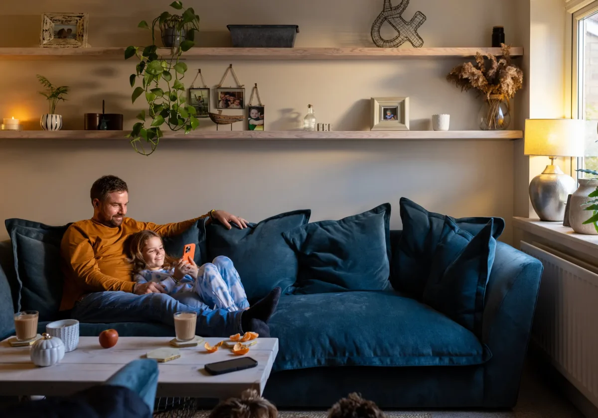 Vater und Tochter sitzen entspannt auf dem Sofa im Wohnzimmer und schauen gemeinsam auf ein Smartphone