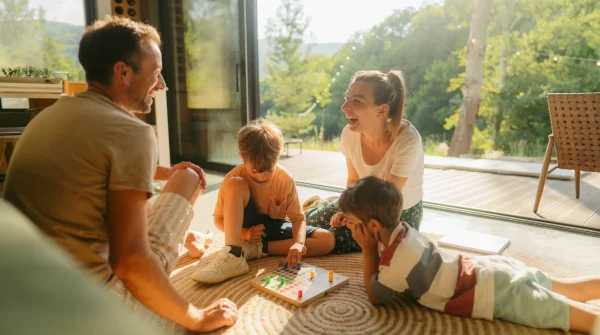 Eine fröhliche Familie sitzt im Wohnzimmer und spielt ein Brettspiel – harmonische Szene in einem modernen, lichtdurchfluteten Zuhause.
