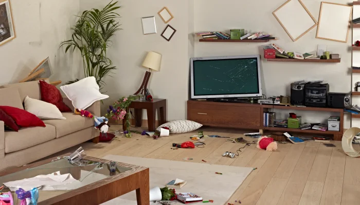Zerstörtes Wohnzimmer nach einem Schaden: zerbrochener Fernseher, kaputtes Mobiliar, Spielzeug und Gegenstände liegen verstreut herum.