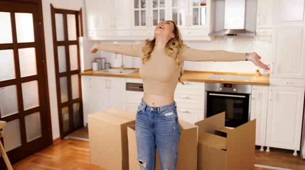 Junge Frau freut sich in neuer Küche mit Umzugskartons – Symbolbild für Hausratversicherung beim Wohnungswechsel