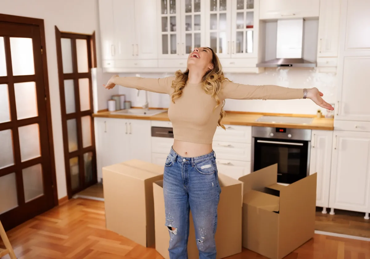 Junge Frau freut sich in neuer Küche mit Umzugskartons – Symbolbild für Hausratversicherung beim Wohnungswechsel