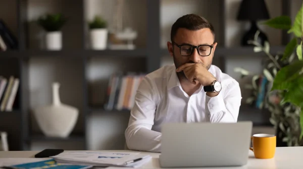 Nachdenklicher Hausverwalter am Schreibtisch vor dem Laptop mit Unterlagen und Kaffeetasse