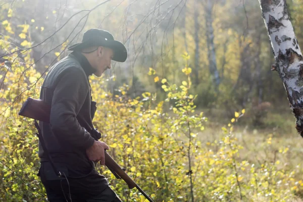 Jäger mit Gewehr im Wald bei Sonnenlicht während eines Streifgangs durch das herbstliche Unterholz
