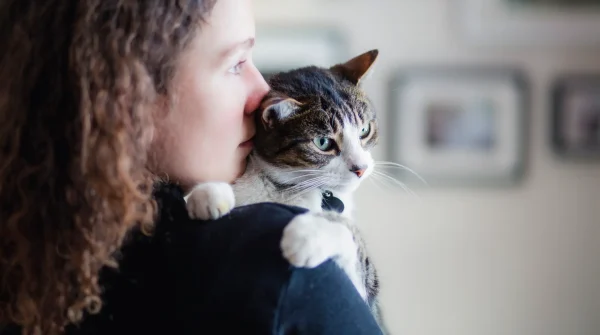 Frau hält eine getigerte Katze liebevoll auf der Schulter – enge Bindung zwischen Mensch und Tier, Fokus auf Fürsorge und Schutz.