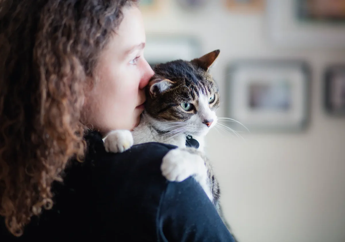 Frau hält eine getigerte Katze liebevoll auf der Schulter – enge Bindung zwischen Mensch und Tier, Fokus auf Fürsorge und Schutz.