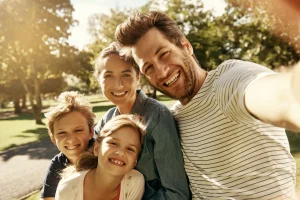 Glückliche Familie mit zwei Kindern macht ein Selfie im Park – Symbolbild für Gesundheit, Vorsorge und Kranken­zusatz­versicherung