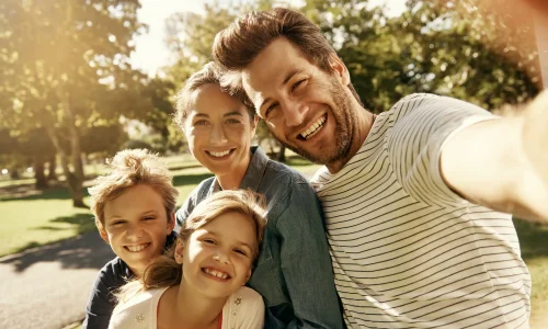 Glückliche Familie mit zwei Kindern macht ein Selfie im Park – Symbolbild für Gesundheit, Vorsorge und Kranken­zusatz­versicherung