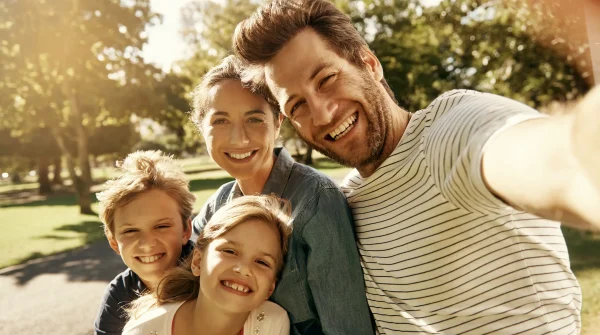 Glückliche Familie mit zwei Kindern macht ein Selfie im Park – Symbolbild für Gesundheit, Vorsorge und Kranken­zusatz­versicherung