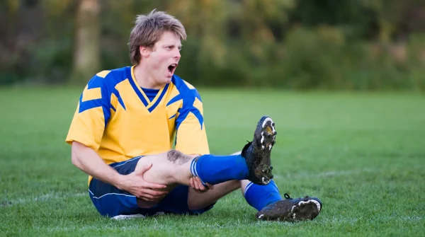 Verletzter Fußballspieler im gelben Trikot greift sich schmerzverzerrt ans Bein – symbolisch für Kreuzbandriss beim Sport