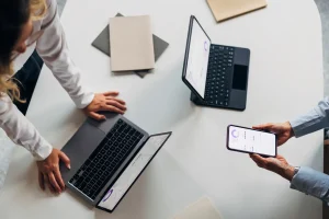 Zwei Personen analysieren digitale Auswertungen auf Laptop, Tablet und Smartphone – symbolisch für moderne Versicherungsberatung.