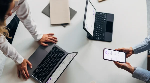 Zwei Personen analysieren digitale Auswertungen auf Laptop, Tablet und Smartphone – symbolisch für moderne Versicherungsberatung.