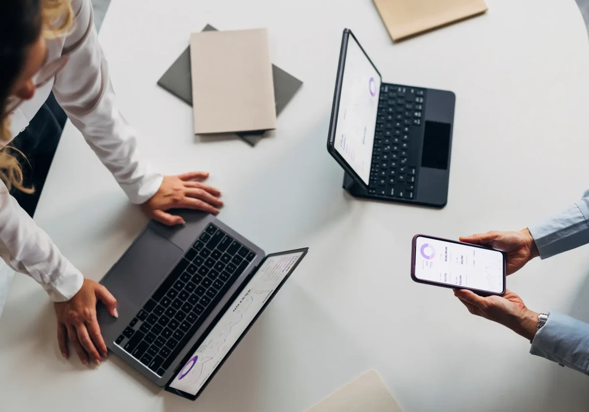Leistungen von uns Zwei Personen analysieren digitale Auswertungen auf Laptop, Tablet und Smartphone – symbolisch für moderne Versicherungsberatung.