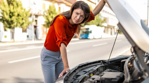 Frau blickt besorgt in offenen Motorraum – Symbolbild für Marderschaden am Auto und unerwartete Reparaturkosten
