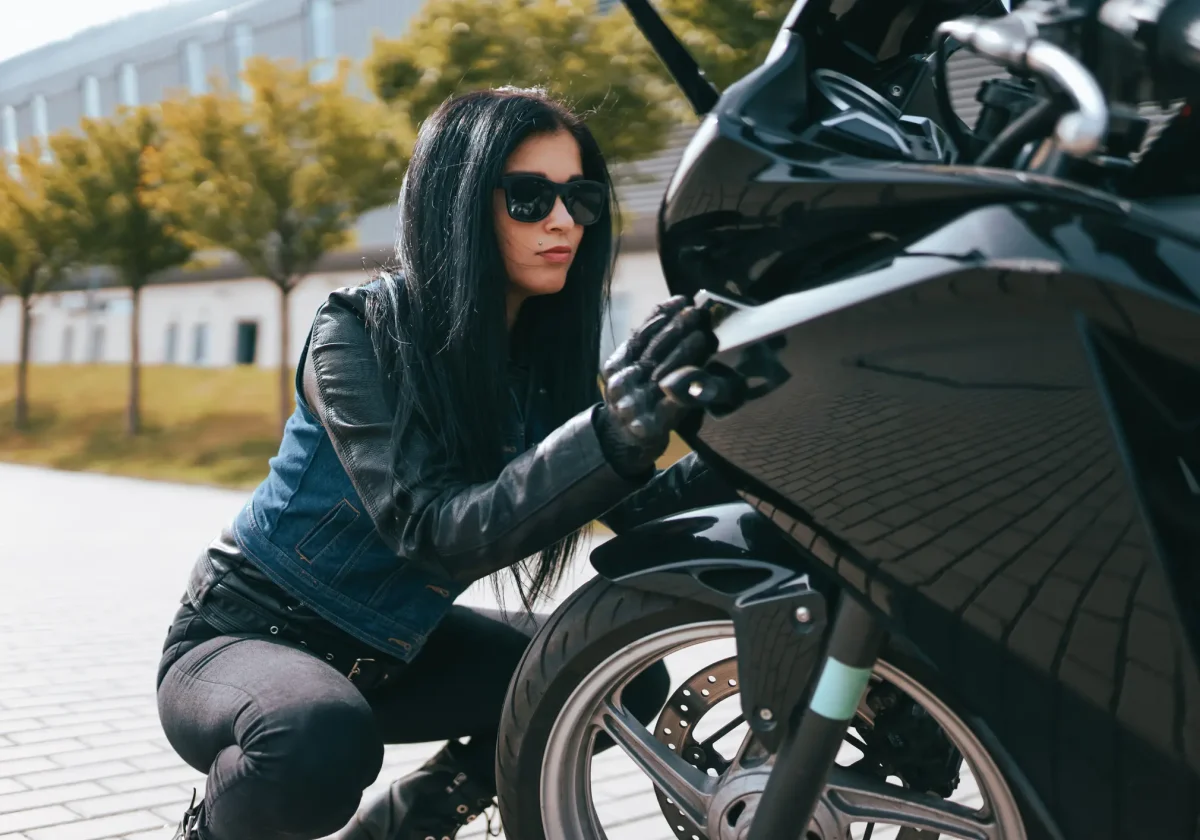 Frau im Lederoutfit prüft ihr Motorrad auf einem Parkplatz – Symbolbild für Motorradversicherung und Sicherheit