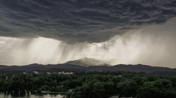 Gewitterfront mit Starkregen und dunklen Wolken über bewaldeter Landschaft und Stadtgebiet