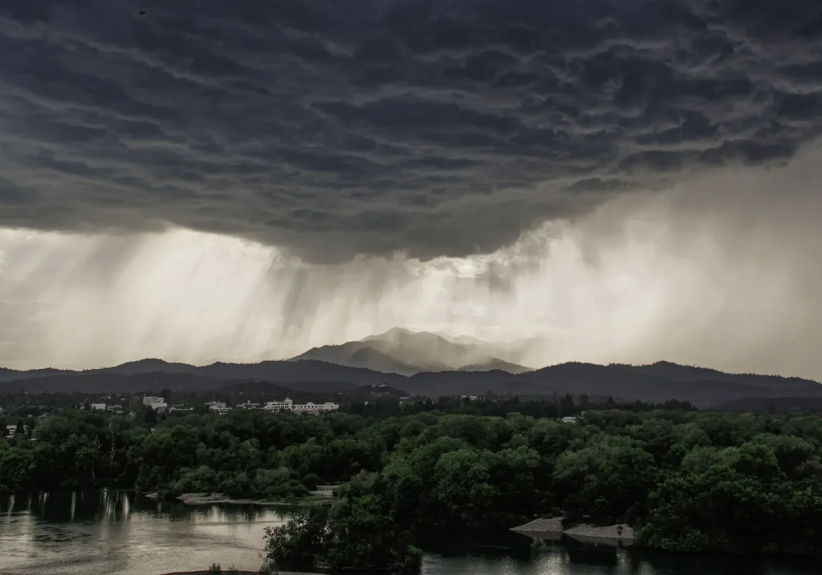 Gewitterfront mit Starkregen und dunklen Wolken über bewaldeter Landschaft und Stadtgebiet