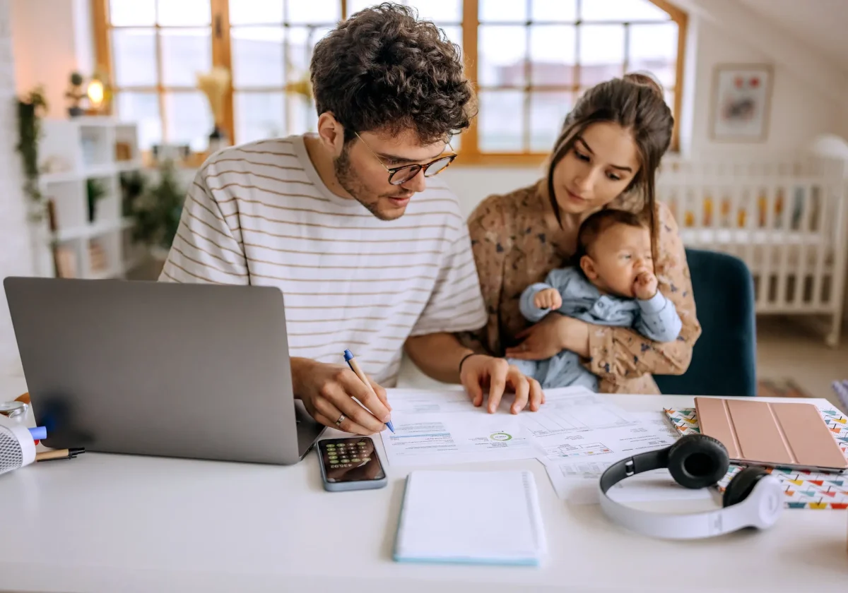 Junges Elternpaar mit Baby prüft Versicherungsunterlagen am Laptop – Planung der Absicherung mit Unfallversicherung im Fokus