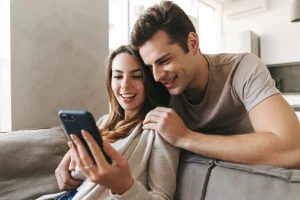 Junges Paar sitzt entspannt auf dem Sofa und schaut gemeinsam auf ein Smartphone