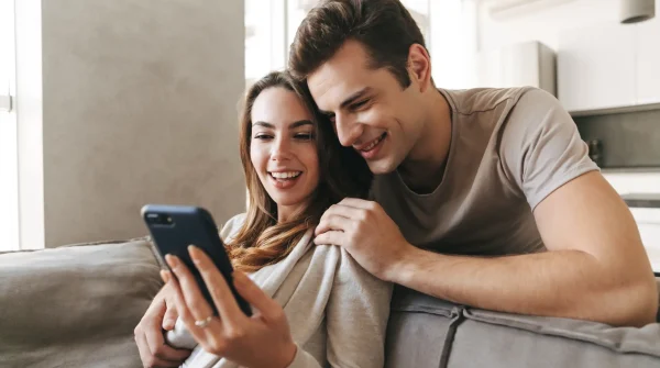 Junges Paar sitzt entspannt auf dem Sofa und schaut gemeinsam auf ein Smartphone