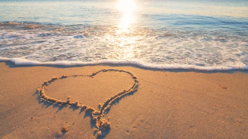Herz im Sand am Strand bei Sonnenuntergang – Symbolbild für entspannte Reisen mit Schutz durch eine passende Reiseversicherung