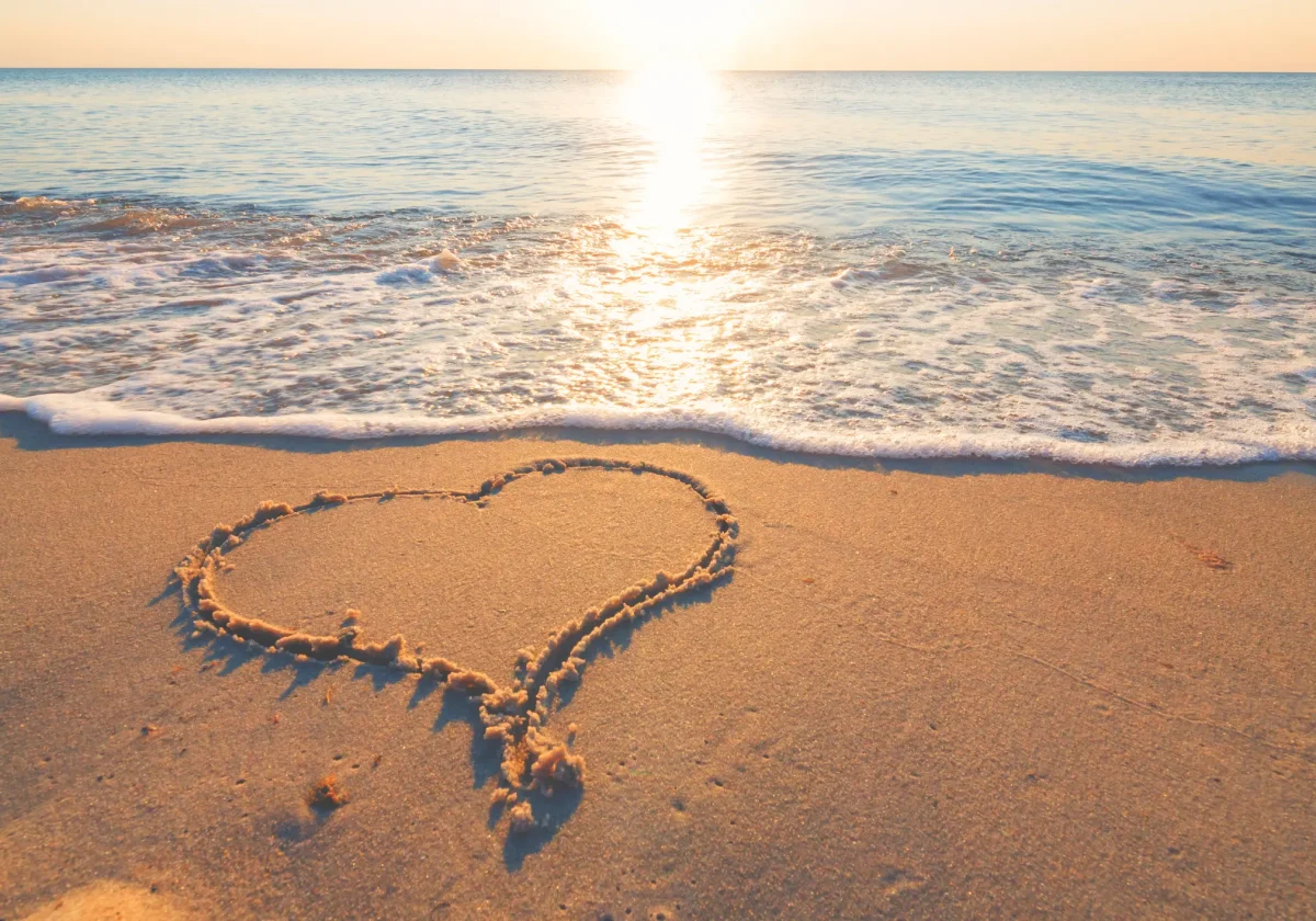 Herz im Sand am Strand bei Sonnenuntergang – Symbolbild für entspannte Reisen mit Schutz durch eine passende Reiseversicherung