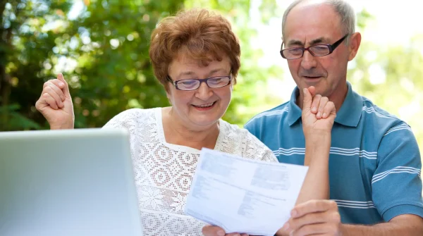 Älteres Paar freut sich über Rentenbescheid vor dem Laptop – Symbolbild für Renteneintrittsalter und Ruhestand