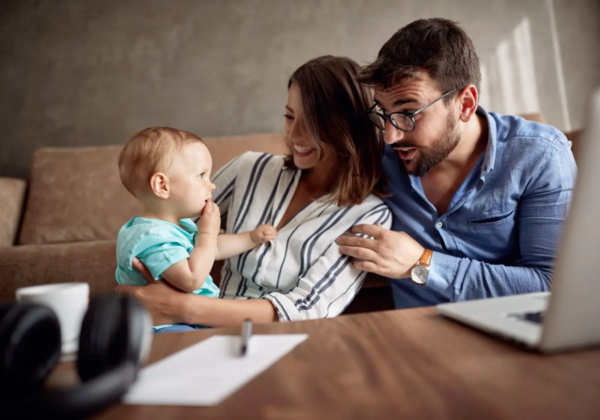 Riester-Rente Junge Familie mit Kleinkind sitzt gemeinsam auf dem Sofa und schaut gespannt auf einen Laptop – Symbol für Zukunftsplanung und Altersvorsorge.