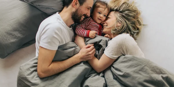 Junge Familie liegt lachend im Bett mit Baby – Symbolbild für Schutz und finanzielle Absicherung durch Risikolebensversicherung
