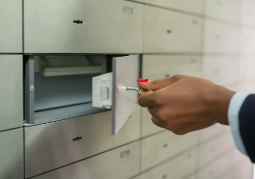 Hand greift mit Schlüssel nach einem geöffneten Schließfach in einem modernen Bankschließfachsystem