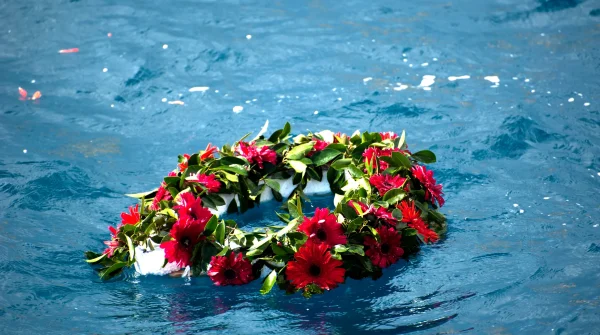 Blumenkranz mit roten Gerbera schwimmt auf ruhigem Meer – symbolisches Bild für eine Seebestattung als besondere Form des Abschieds