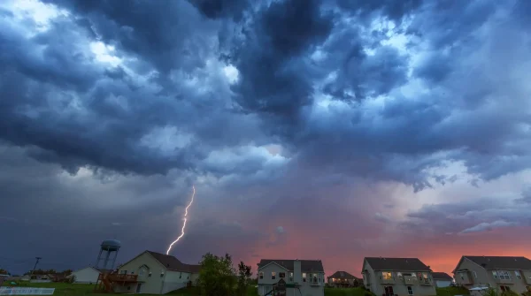 Gewitterhimmel mit Blitzeinschlag über Wohnsiedlung bei Sonnenuntergang (77 Zeichen)