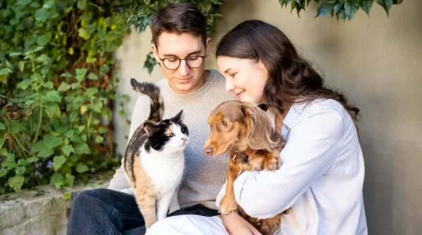Paar sitzt mit Hund und Katze im Garten – symbolisches Bild für Liebe zum Tier und Absicherung durch passende Tierversicherung