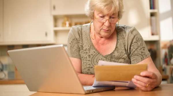 Ältere Frau prüft Unterlagen am Tisch mit Laptop – symbolisch für finanzielle Vorsorge und Verwaltung eines Treuhandkontos für Bestattung
