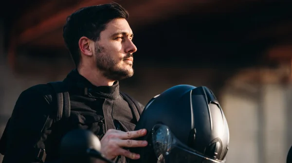 Motorradfahrer mit schwarzer Schutzkleidung hält seinen Helm in der Hand und blickt konzentriert in die Ferne – Unfallschutz