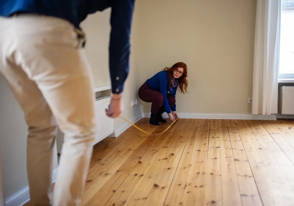 Paar misst mit Maßband den leeren Raum aus – Symbolbild für Wohnfläche und Unterversicherungsverzicht bei der Hausratversicherung