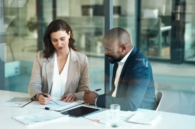 Zwei Geschäftsleute im Gespräch am Konferenztisch mit Unterlagen – Beratung zu finanziellen Risiken und Absicherung im Büro