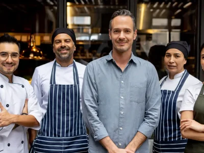 Team eines Restaurants mit Koch, Servicekraft und Inhaber posiert gemeinsam vor dem Eingang