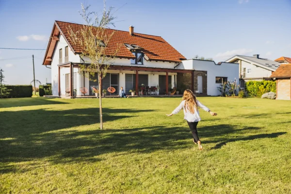 Mädchen läuft über eine Wiese auf ein modernes Einfamilienhaus mit Terrasse und Garten zu