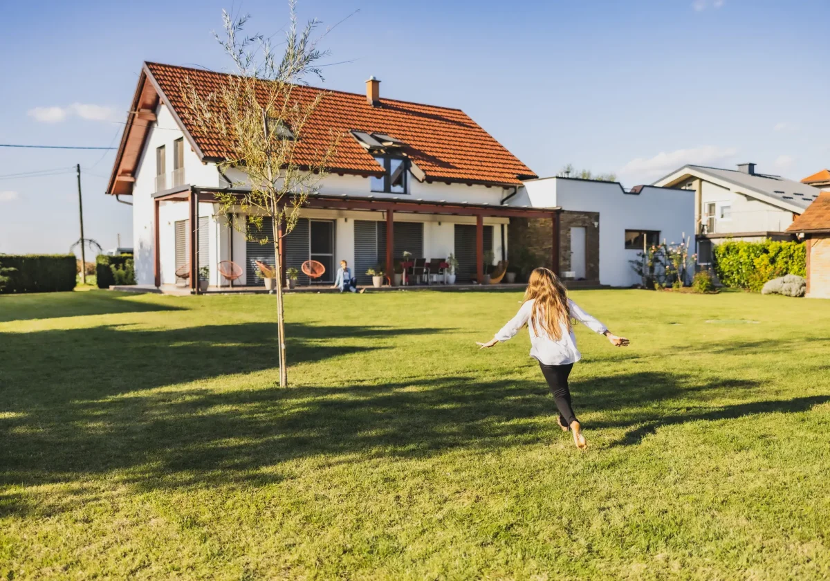 Mädchen läuft über eine Wiese auf ein modernes Einfamilienhaus mit Terrasse und Garten zu