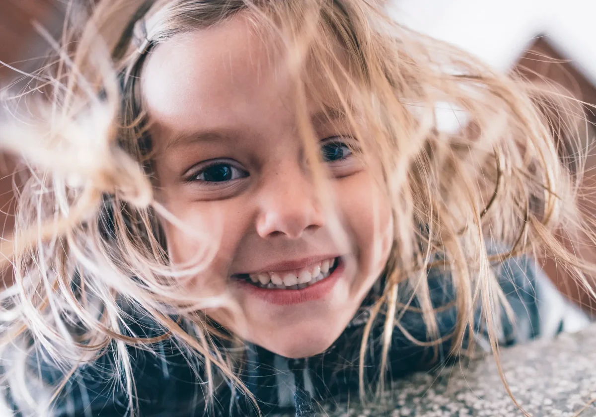 Zahnzusatzversicherung-Kinder Lachendes Kind mit gesunden Zähnen und wehenden Haaren – Symbol für unbeschwertes Aufwachsen mit guter Zahnvorsorge