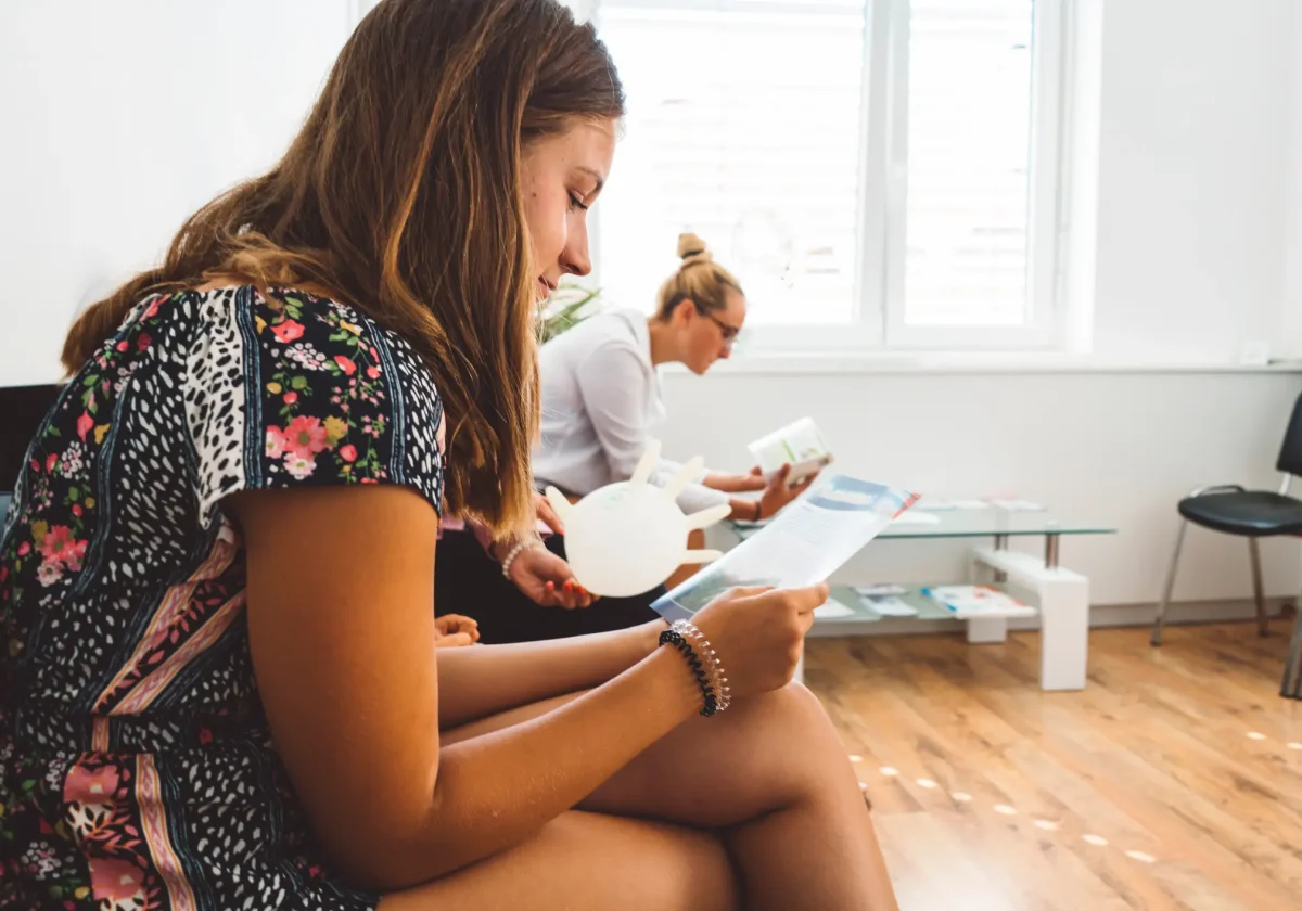 Patientinnen im Wartezimmer einer Zahnarztpraxis, vertieft in Informationsbroschüren – Vorbereitung auf ein Beratungsgespräch.