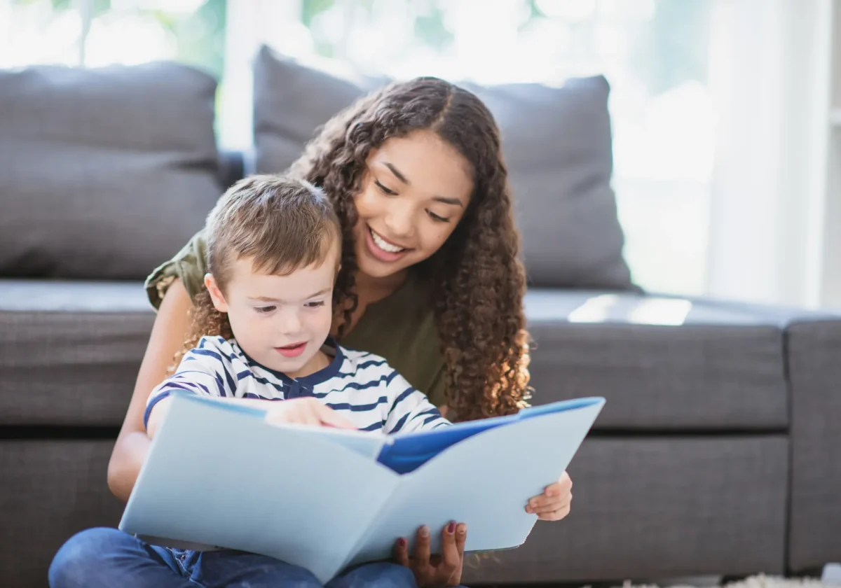 Au-pair-Mädchen liest mit einem kleinen Jungen ein Buch auf dem Sofa – Symbolbild für Betreuung und Au-pair-Versicherung im Alltag