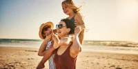 Fröhliche Familie spielt mit ihrem Kind am Strand bei Sonnenschein während eines Urlaubs am Meer