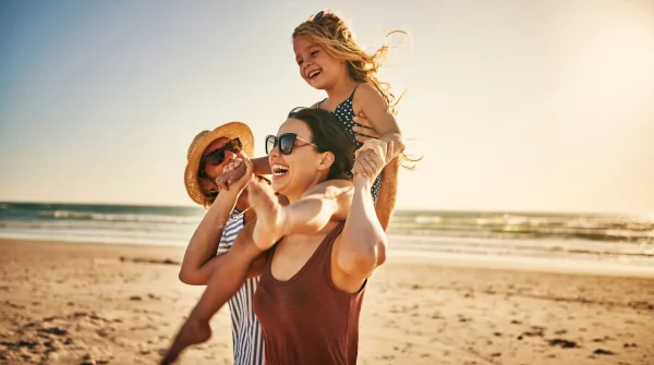 Fröhliche Familie spielt mit ihrem Kind am Strand bei Sonnenschein während eines Urlaubs am Meer